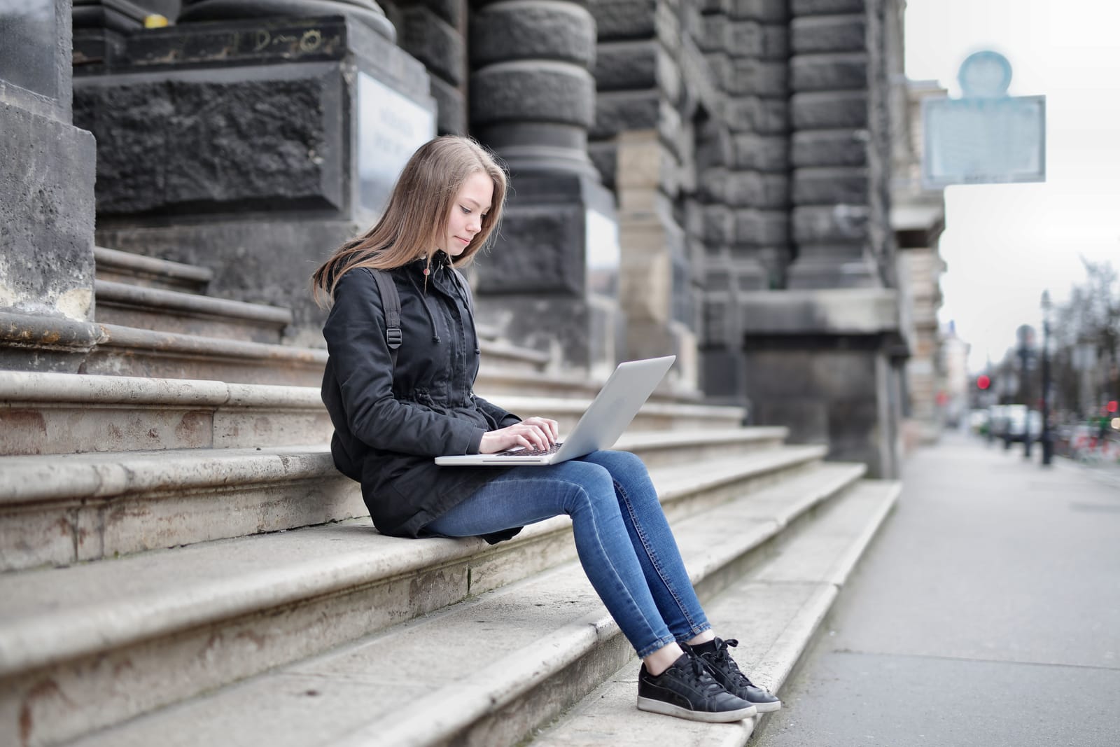 A student working on a laptop on the steps of a grand old building